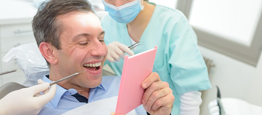 Man in dental chair admiring treatment results with dentist looking over shoulder