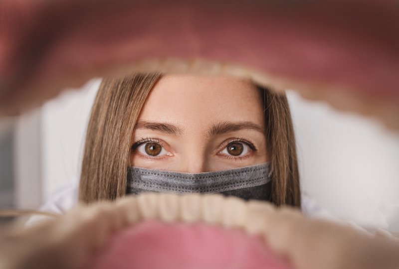 A view of a mask-wearing dentist through a patient’s open mouth